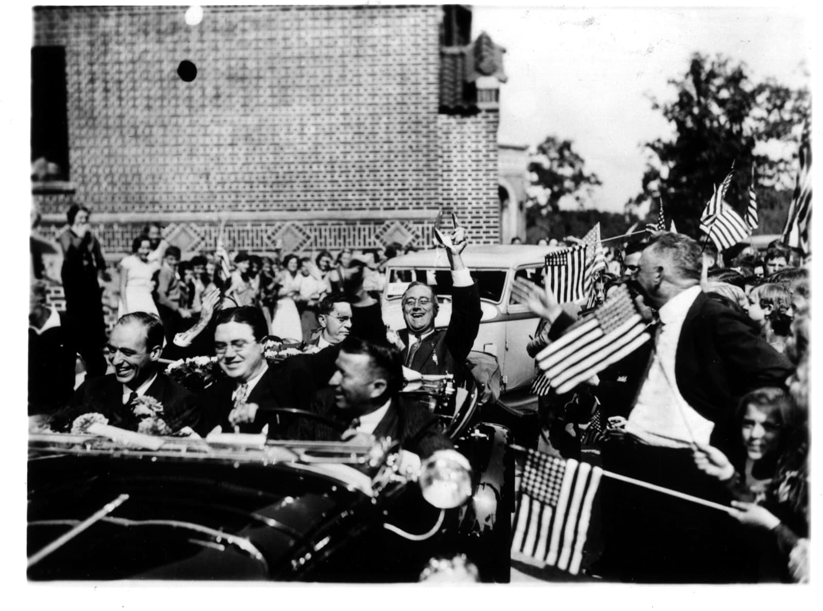 Franklin D. Roosevelt riding in an open car through a crowd waving American flags during the 1936 campaign.